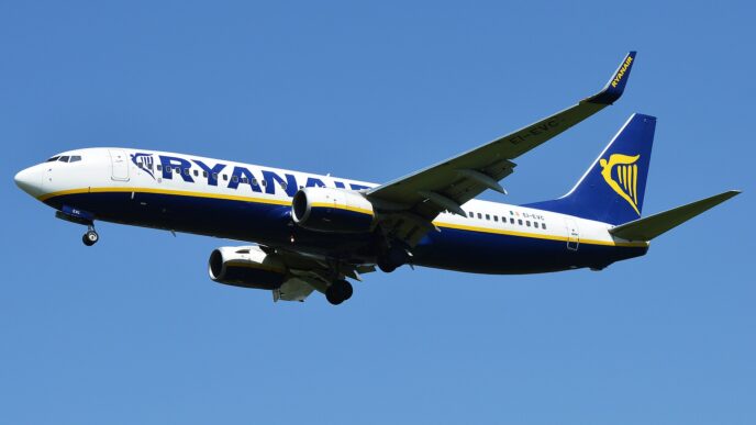 Boeing 737 linii Ryanair w niebiesko-żółtych barwach z wypuszczonym podwoziem podchodzi do lądowania na tle błękitnego nieba.