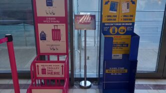 Dwa metalowe stojaki do mierzenia bagażu podręcznego w terminalu lotniska: różowy Wizz Air i niebieski Ryanair.