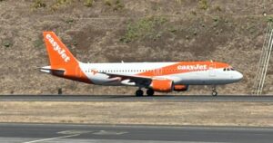 Samolot Airbus A320 w pomarańczowo-białych barwach easyJet kołuje po pasie startowym na tle zbocza porośniętego suchą trawą