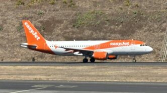 Samolot Airbus A320 w pomarańczowo-białych barwach easyJet kołuje po pasie startowym na tle zbocza porośniętego suchą trawą