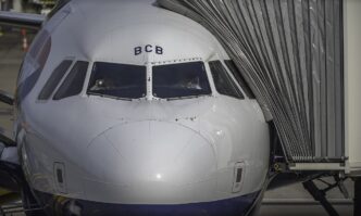 Przód samolotu pasażerskiego z widocznym kokpitem i dwoma pilotami, przy rękawie pasażerskim