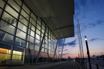 Szklana elewacja terminalu lotniska we Wrocławiu o zmierzchu, wózki bagażowe przy wejściu i podjazd dla samochodów