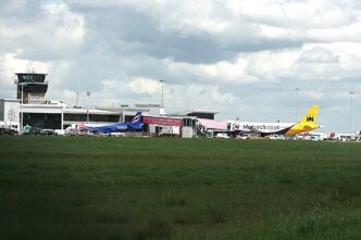 Terminal lotniska Leeds Bradford z wieżą kontroli lotów, przed budynkiem stoją samoloty, na pierwszym planie trawiaste pole