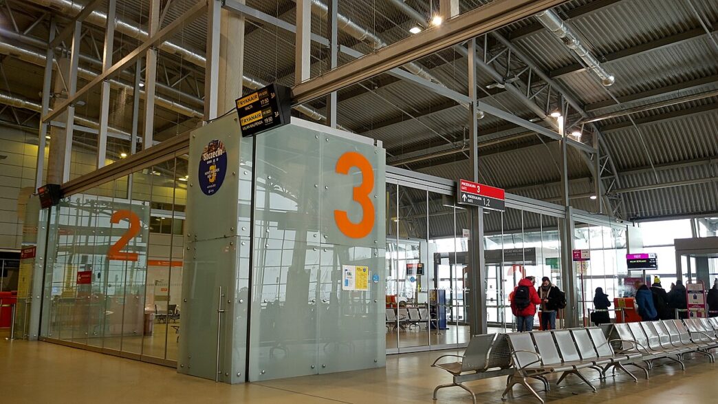 Hala odlotów z bramkami numer 2 i 3, rzędem foteli i pasażerami czekającymi przy wyjściu