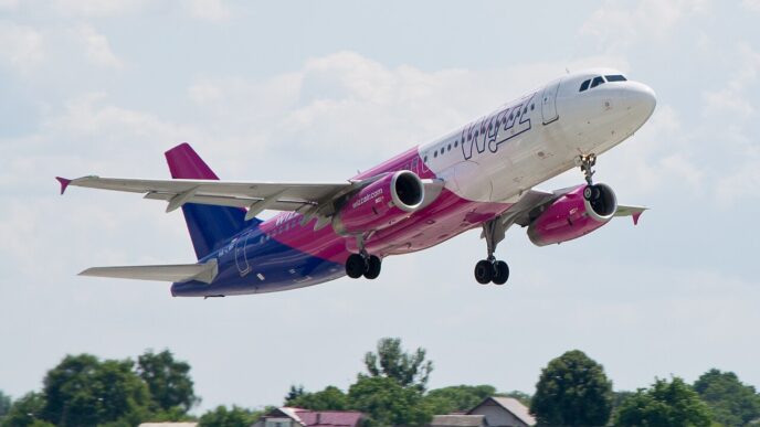 Samolot Airbus A320 w biało-fioletowo-różowych barwach Wizz Air wznosi się nad polami i zabudowaniami